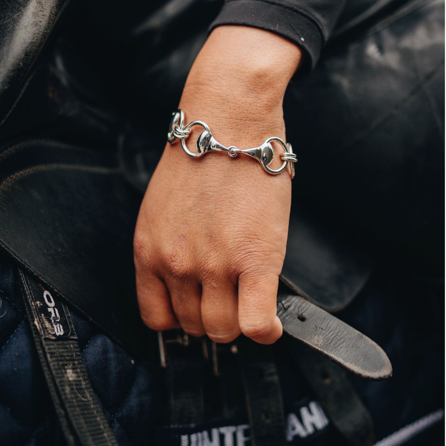 A horse rider adjusting a horses girth while wearing a Crawford Hill Equestrian Jewellery three snaffle horse bit bracelet paired with a horse bit snaffle ring.